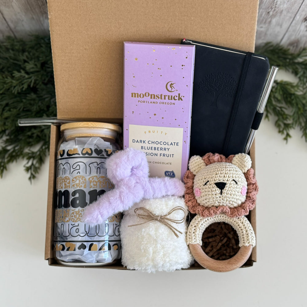 A curated gift box set containing a jar of 'mamamoon' brand coconut sugar, a purple Moonstruck chocolate bar, a black notebook, a lavender plush toy, a white fluffy pouch, and a crocheted lion teether.