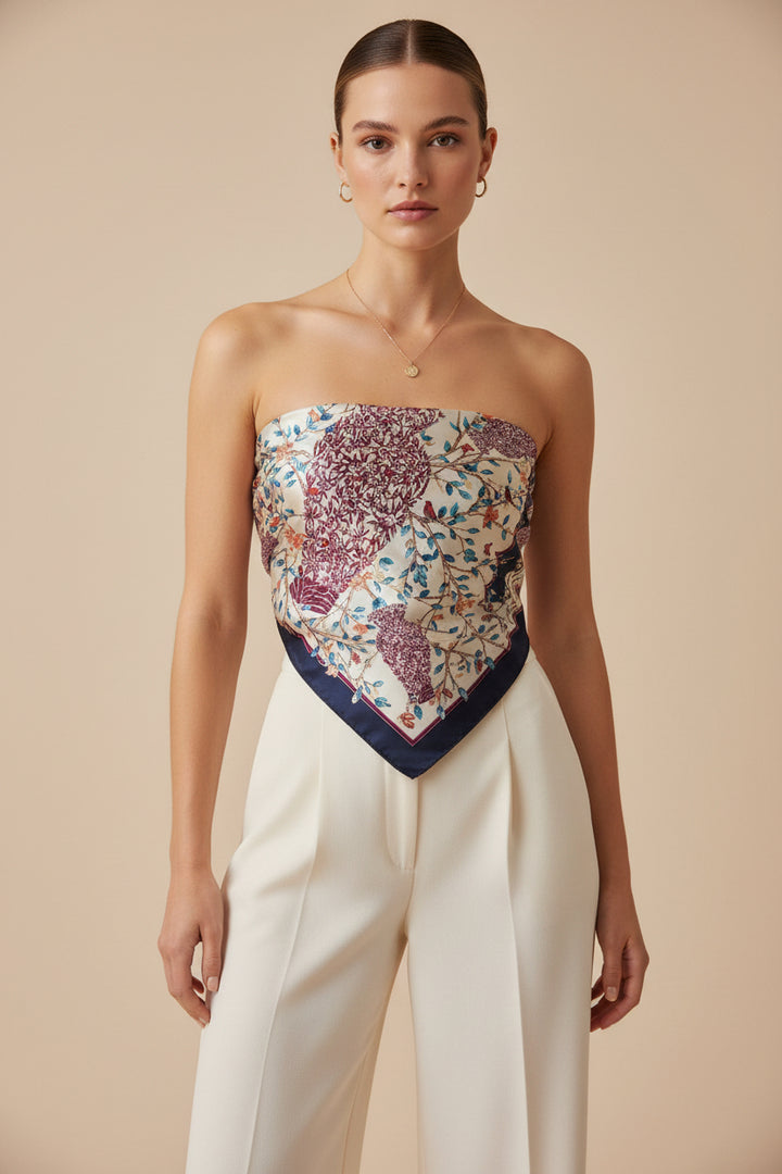 A model wearing a strapless bandeau top with a floral and paisley pattern in purple, blue, and beige, paired with cream-colored wide-leg trousers, set against a solid beige background.