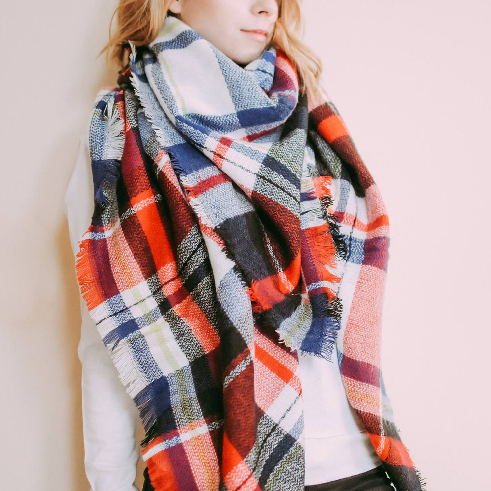 A person wearing a multicolored tartan plaid scarf with fringed ends, wrapped around the neck and shoulders.