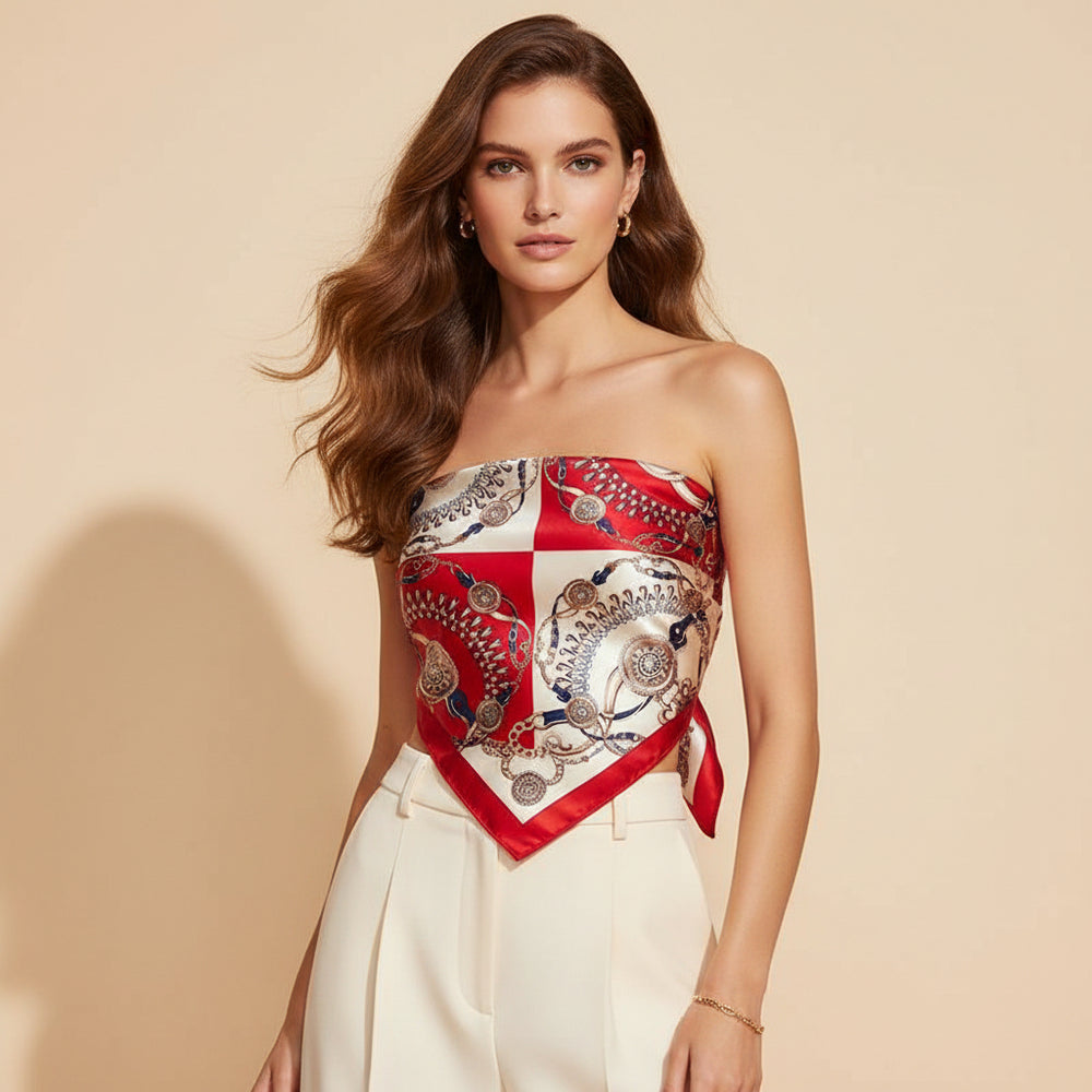A woman modeling a strapless bandeau-style top made from a square silk scarf with a red, white, and metallic gold paisley print, paired with cream-colored trousers, set against a solid beige background.