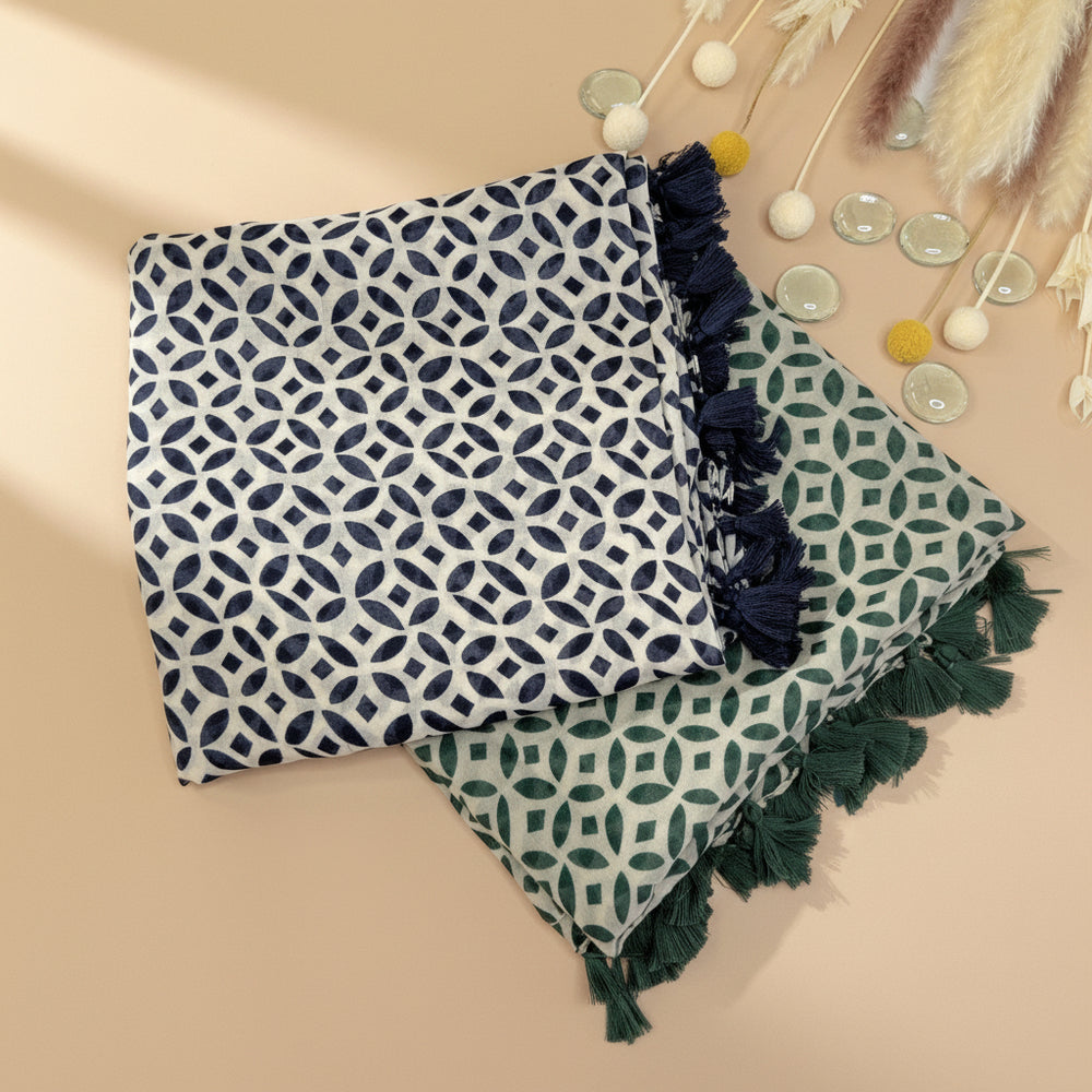 Two scarves with geometric patterns, one navy and one green, laid out flat with fringed edges, on a white background with decorative items.