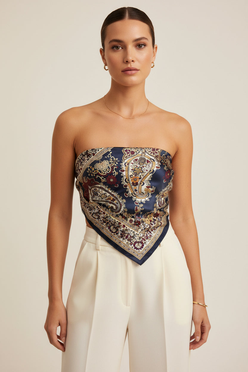 A woman modeling a strapless bandeau top made from a navy blue paisley silk scarf, paired with white trousers, against a warm beige studio background.