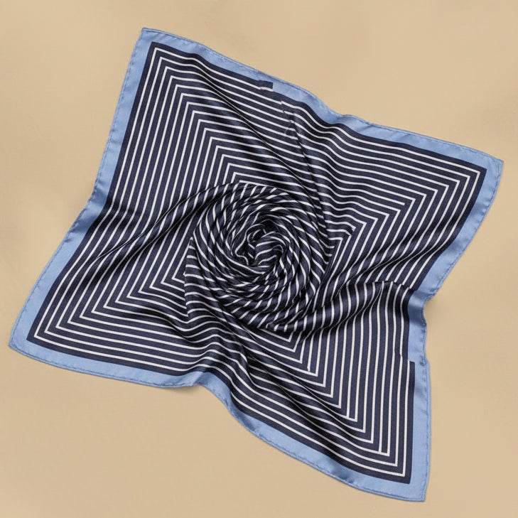 A gray silk bandana with a geometric pattern displayed on a white background, alongside a dry plant decoration.