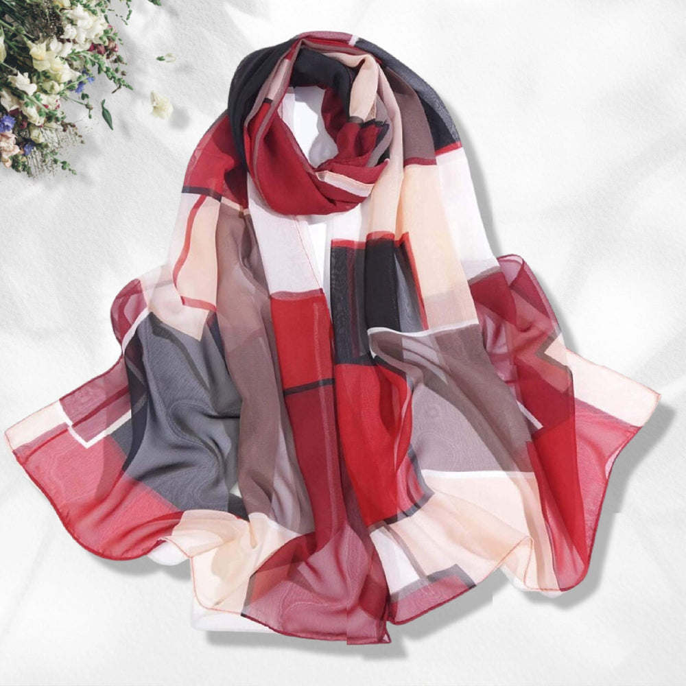 A long, silky, red chiffon scarf with geometric patterns, displayed on a white surface with a floral arrangement in the background.