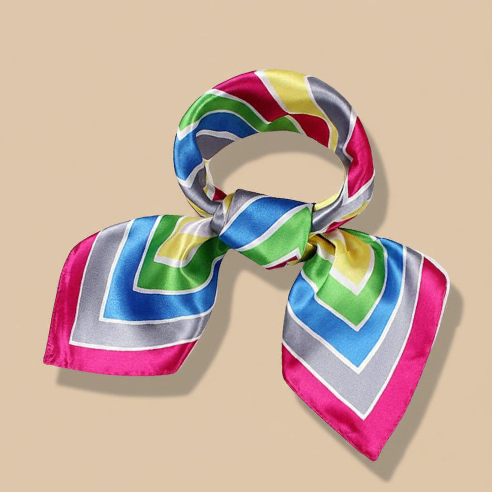 A multicolored geometric patterned silk scarf tied in a bow, displayed on a white background with dried plant stems in the foreground.